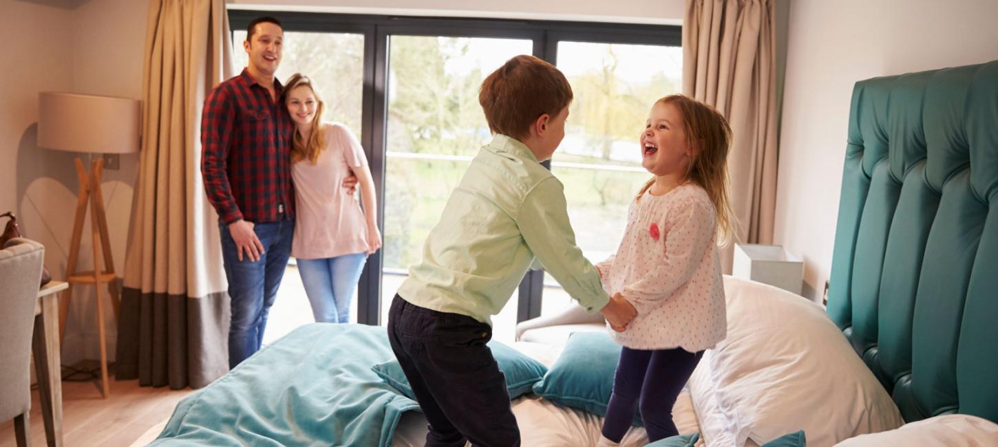 Two children are having fun jumping on the bed, while their mum and dad enjoy watching them. LEGOLAND® Billund Resort has plenty of different places to stay.