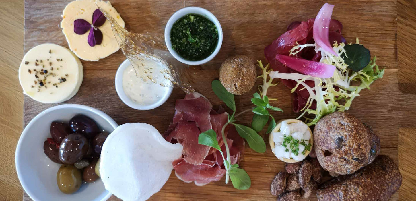 Anretning med lokale specialiteter som oste, oliven, skinke og dips set ovenfra.