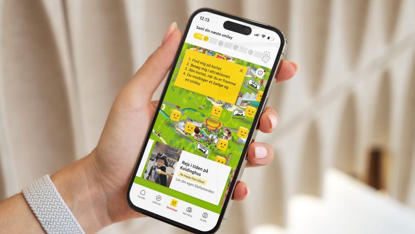 En hånd der holder en mobiltelefon, som viser LEGOLAND Billund Resort resortmap med skattejagten