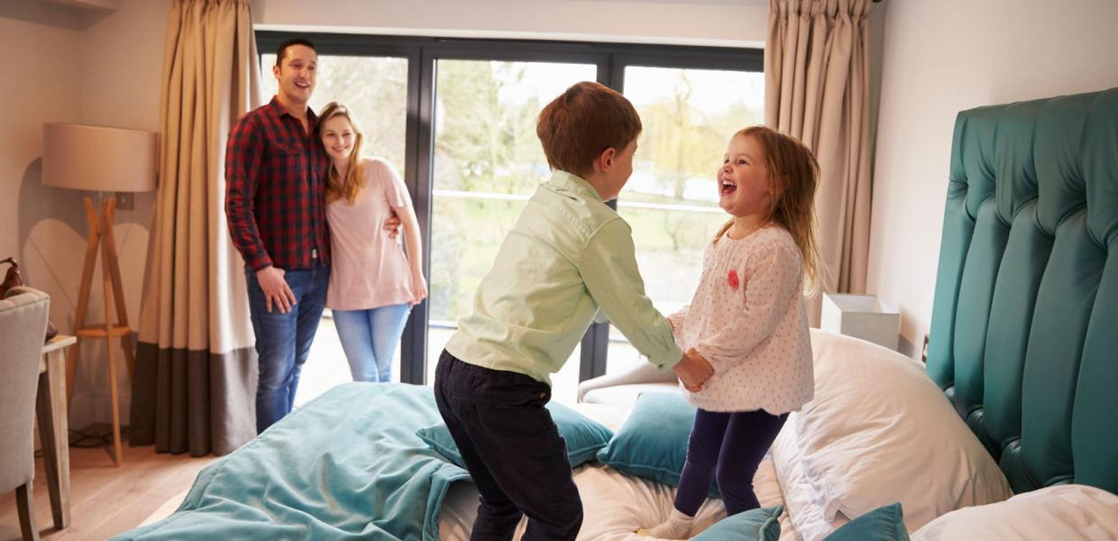 Two children are having fun jumping on the bed, while their mum and dad enjoy watching them. LEGOLAND® Billund Resort has plenty of different places to stay.