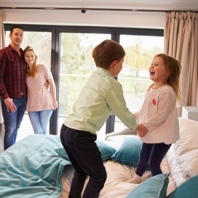 Two children are having fun jumping on the bed, while their mum and dad enjoy watching them. LEGOLAND® Billund Resort has plenty of different places to stay.